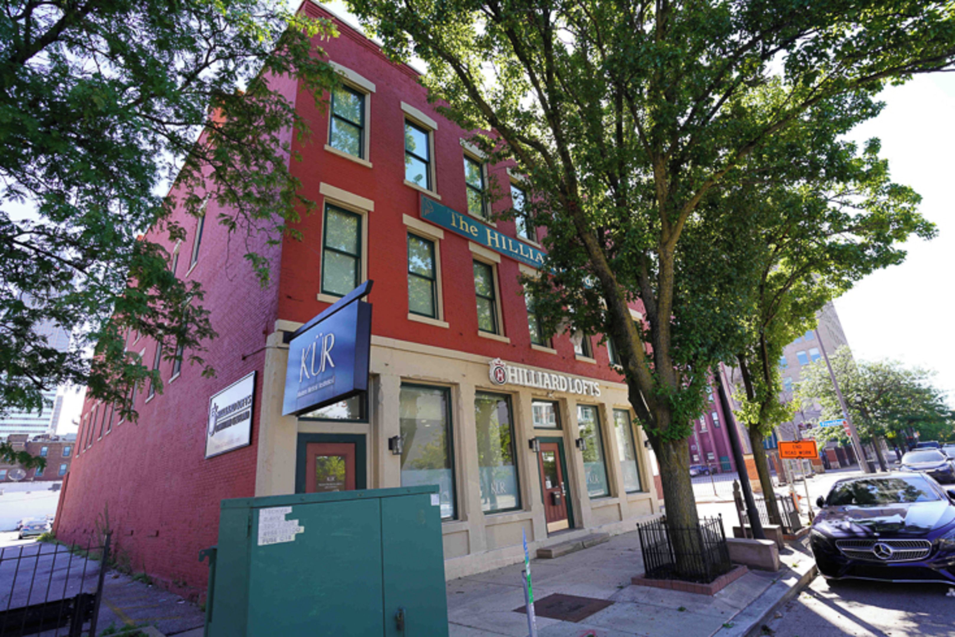 A red brick building with a storefront named 'HILLIARD LOFTS' and a sign for 'KUR' above it.