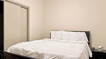 A single bed with white bedding in a room with a closed door and a nightstand with a tissue box.