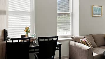 A living room with a sofa, a dining table with chairs, and a window with blinds.