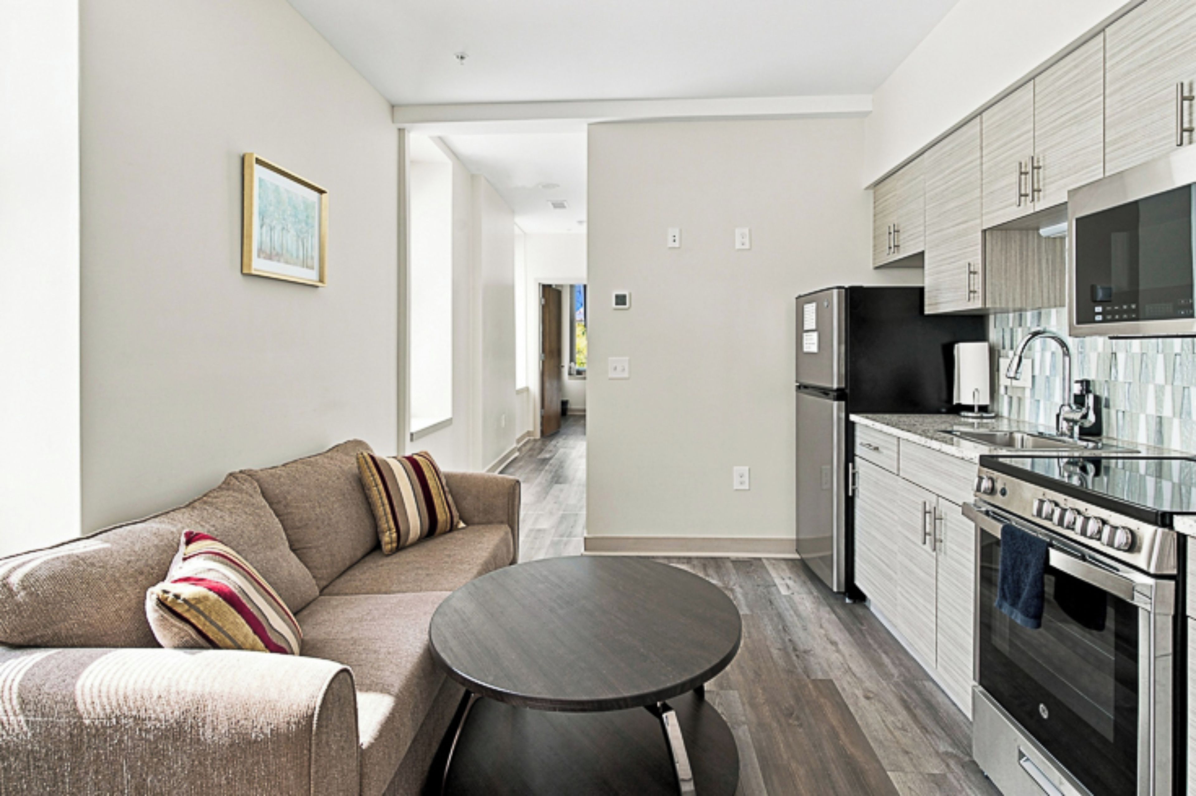 A modern kitchen with stainless steel appliances, a dining area with a round table, and a living room with a sofa.