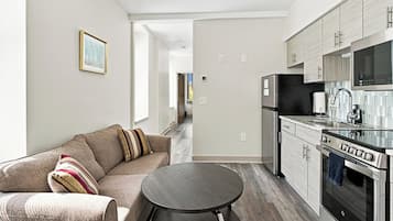 A modern kitchen with stainless steel appliances, a dining area with a round table, and a living room with a sofa.