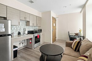 A compact kitchen with modern appliances, a dining area with a dark round table, and a sofa with striped cushions.