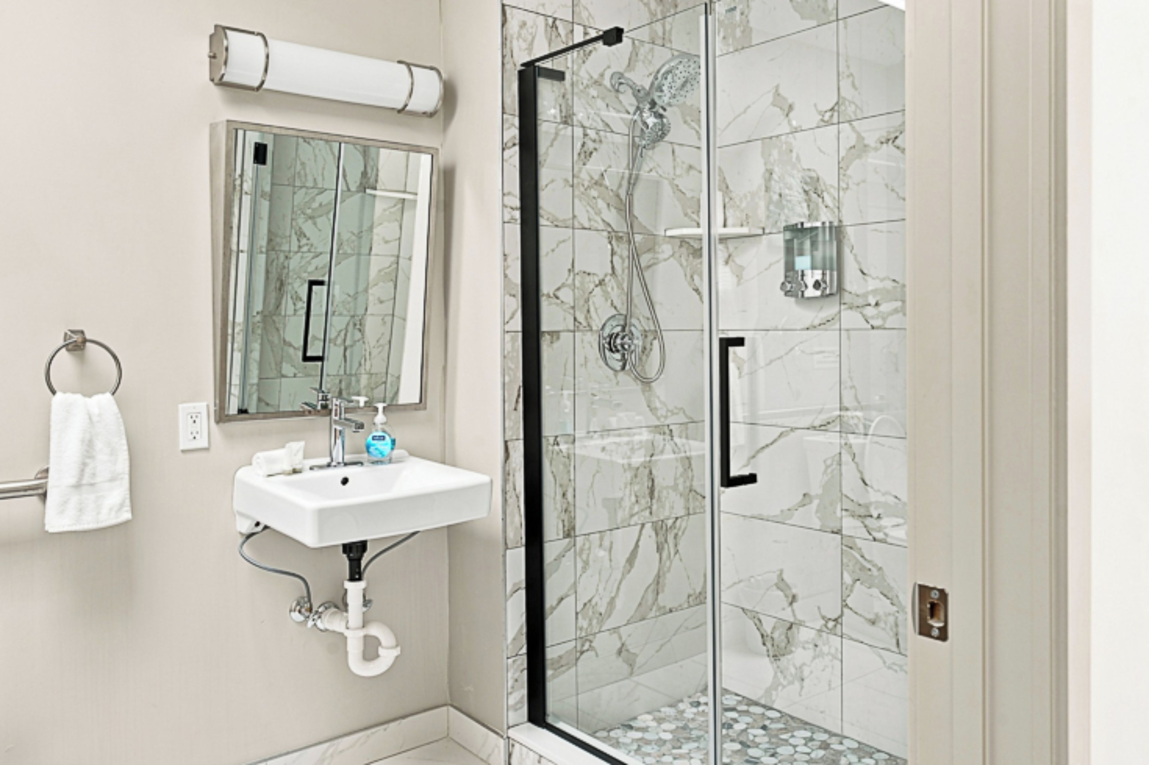 A bathroom with a glass-enclosed shower, a sink with a mirror above it, and a towel hanging on a rack.