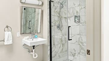 A bathroom with a glass-enclosed shower, a sink with a mirror above it, and a towel hanging on a rack.