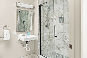 A bathroom with a glass-enclosed shower, a sink with a mirror above it, and a towel hanging on a rack. - Downtown Historic Warehouse District Lofts 307 (Cleveland)