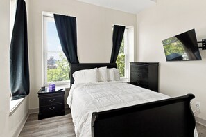 A bedroom with a bed, nightstands, a dresser, and a window with curtains. - Downtown Historic Warehouse District Lofts 307 (Cleveland)