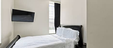 Ein Schlafzimmer mit einem Bett, einem Nachttisch, einer Wandregal und einem Fenster mit Vorhängen.