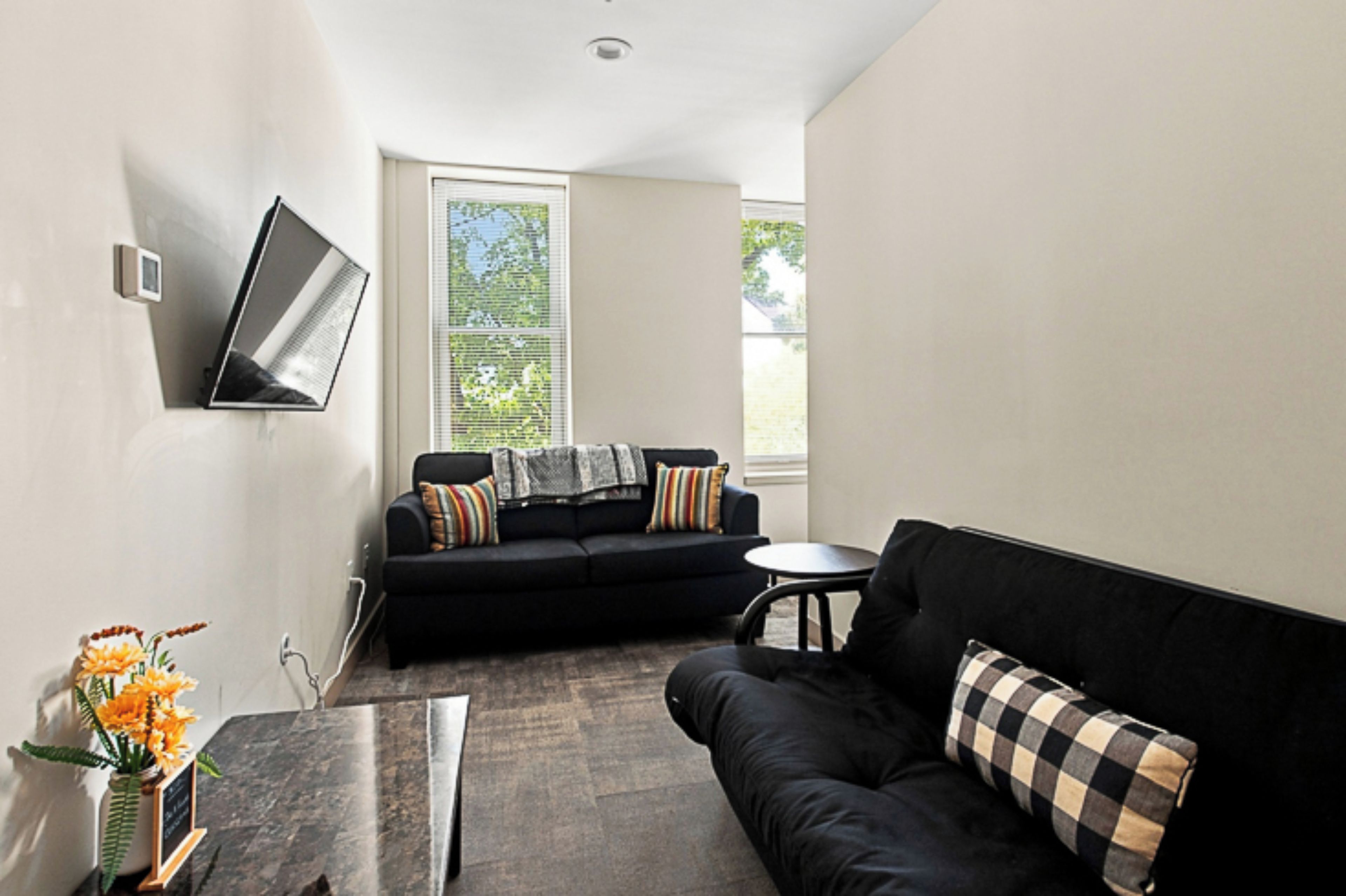 A modern living room with a black sofa, a small round table, and a flat-screen TV mounted on the wall.
