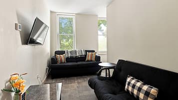 A modern living room with a black sofa, a small round table, and a flat-screen TV mounted on the wall.
