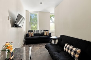 A modern living room with a black sofa, a small round table, and a flat-screen TV mounted on the wall. - Downtown Historic Warehouse District Lofts 209 (Cleveland)