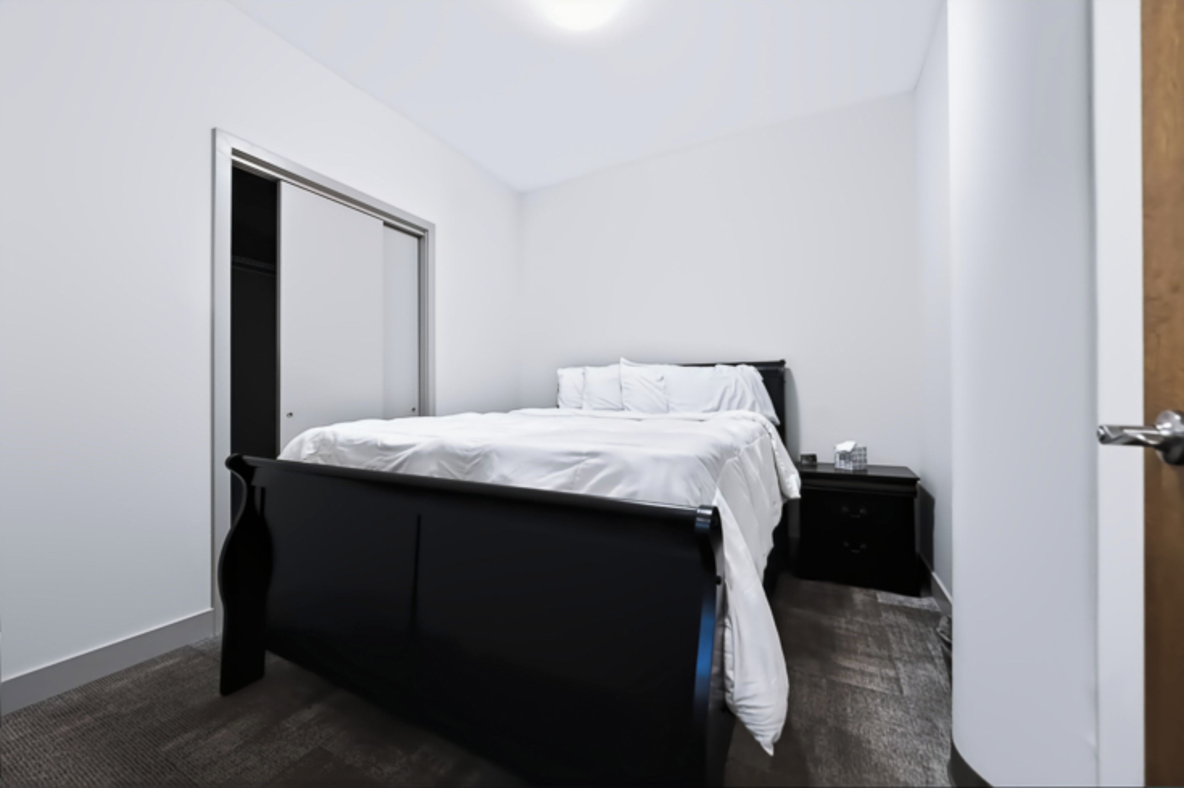 A bedroom with a bed, a nightstand, and a door.