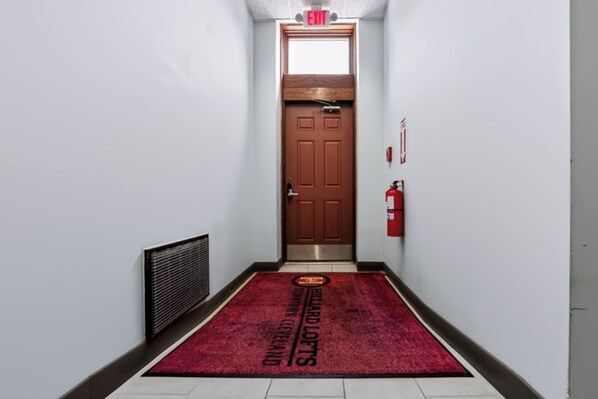 A hallway with a red carpet, a brown door, and a fire extinguisher on the wall.