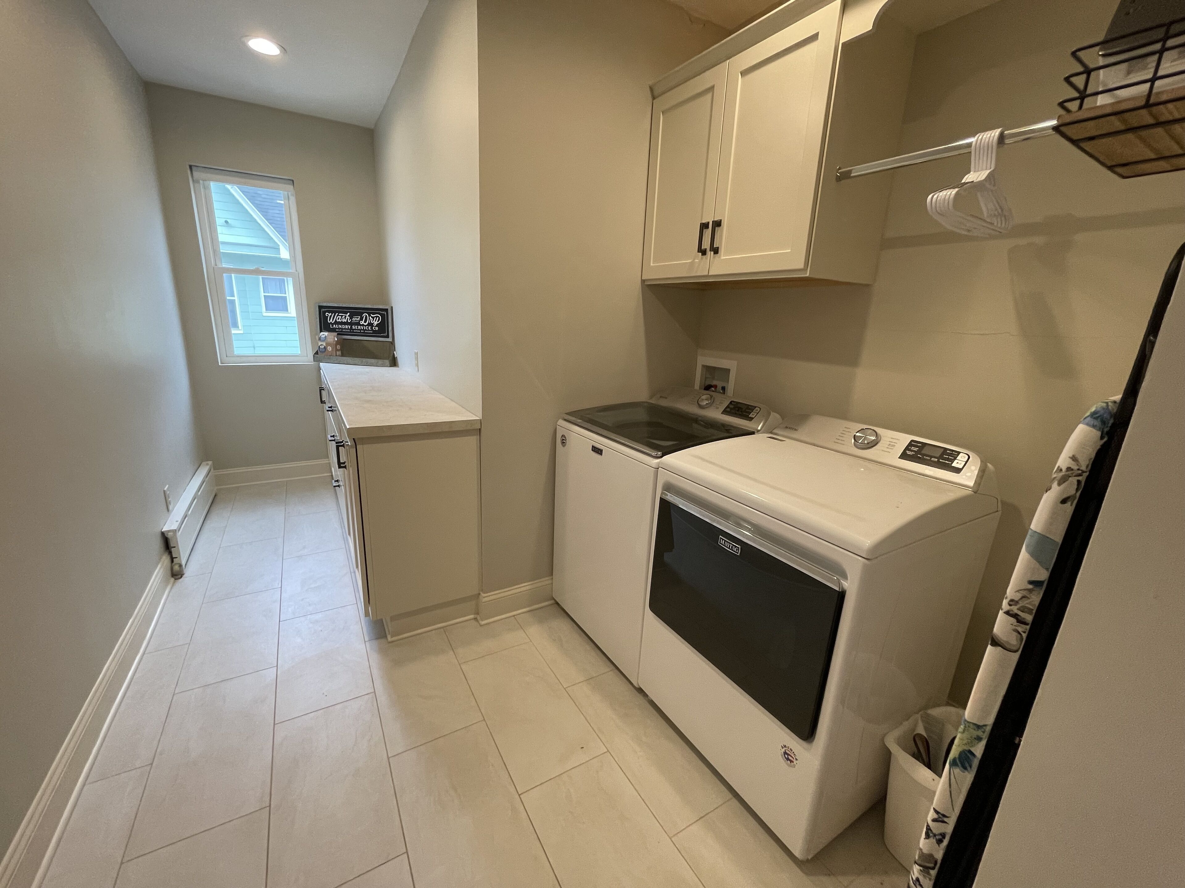 A laundry room with a washer and dryer, a small window, and a sign for a laundry service.