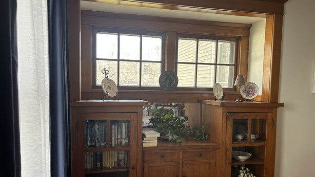 Un meuble en bois doté de portes en verre, contenant des livres et des assiettes décoratives.