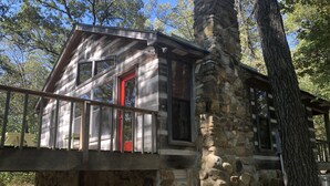 Une cabane en pierre avec une porte rouge, de grandes fenêtres et une terrasse en bois.