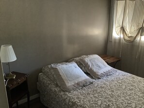 A bedroom with a bed, a nightstand, a lamp, and a window with curtains. - Beautiful apartment 500 meters from the ocean (Six-Fours-les-Plages)