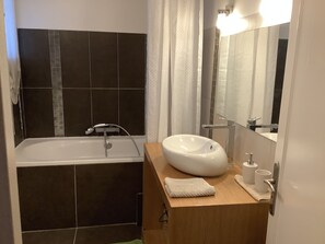 A bathroom with a bathtub, a sink, a mirror, and a towel on the counter. - Beautiful apartment 500 meters from the ocean (Six-Fours-les-Plages)