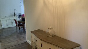 Una habitación con un aparador de madera, un florero de cristal y una zona de comedor al fondo.
