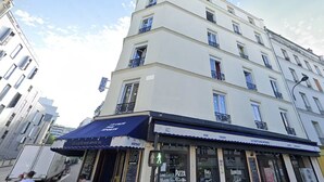 A multi-story building with a flat facade, balconies, and a ground-level bar with a blue awning.