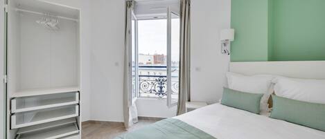 A bedroom with a bed, a wardrobe, and a view of the city through a balcony.