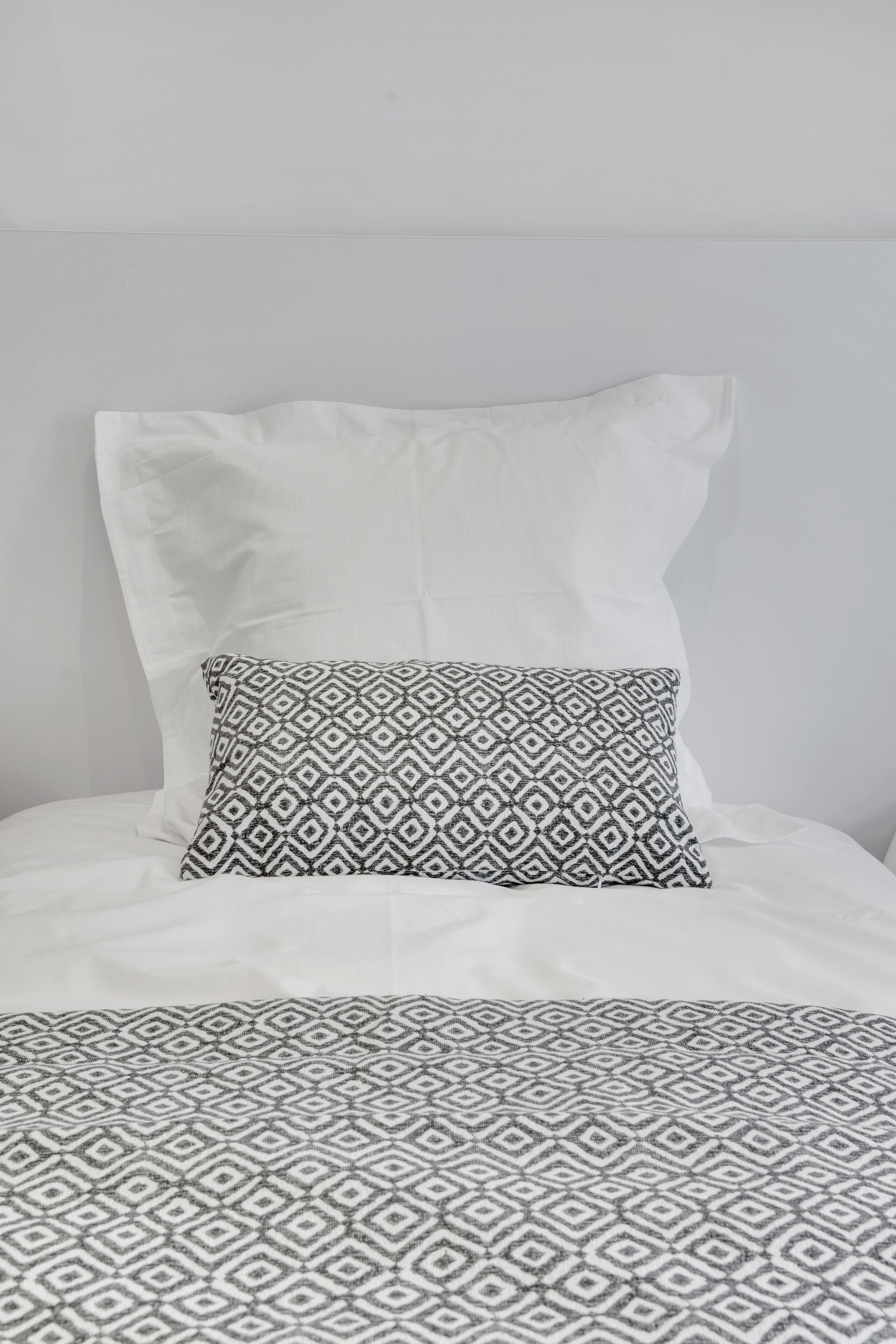 A bed with a patterned bedspread and two pillows, one plain and one with a geometric design.