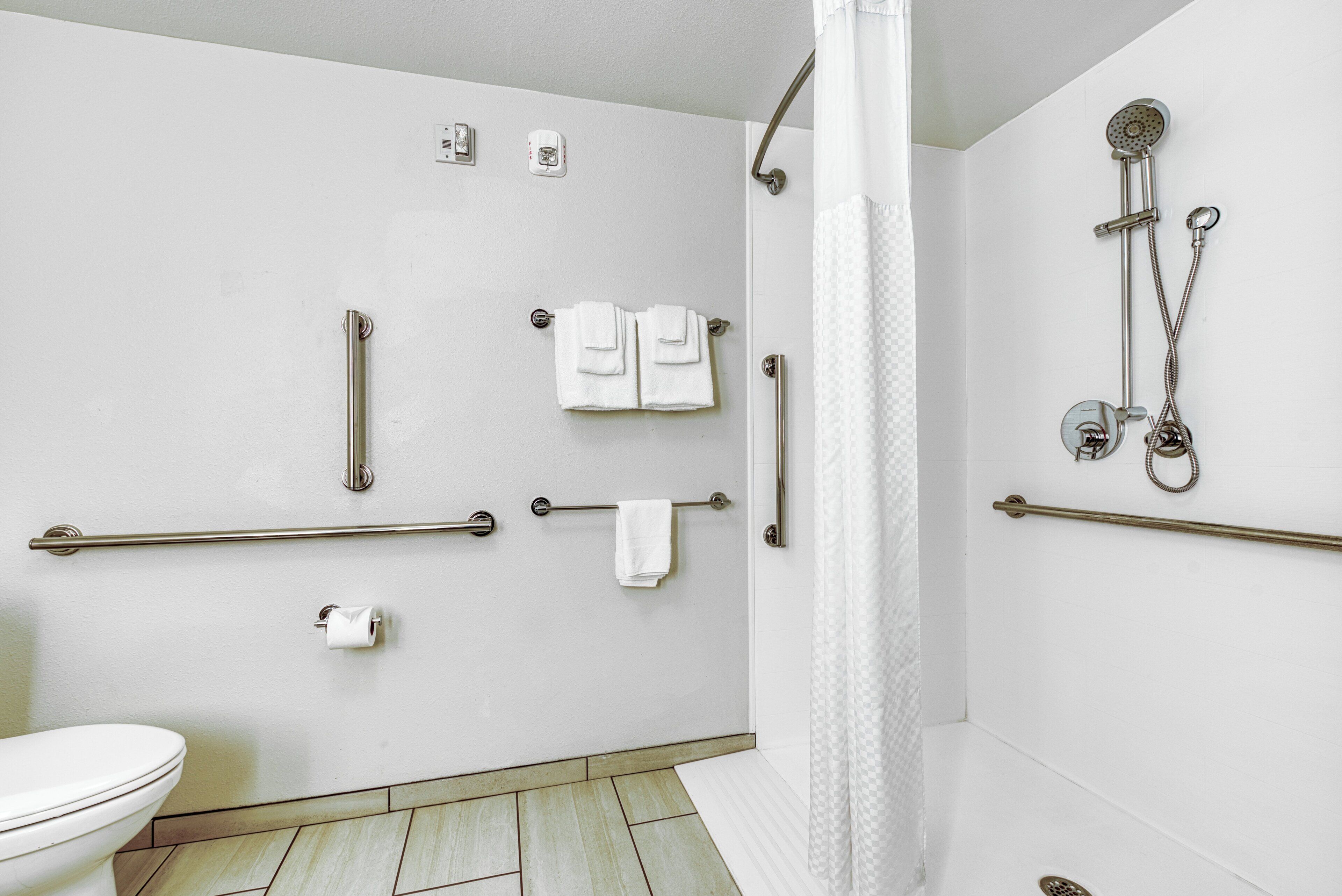 A bathroom with a toilet, grab bars, a shower with a handheld showerhead, and a towel rack.