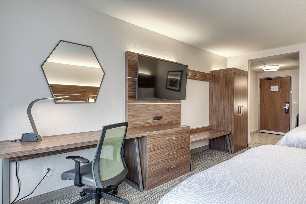 Habitación de hotel con escritorio de madera, televisor de pantalla plana, espejo, cama y armario.