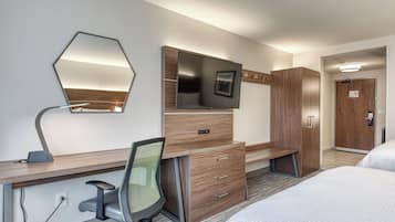 A hotel room with a bed, a desk with a chair, a television, a wardrobe, and a mirror.
