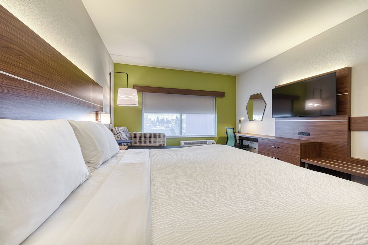 Habitación de hotel con una cama grande, un escritorio, una silla, un televisor y una ventana con persianas.
