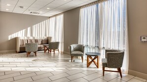 A hotel room with a sofa, two armchairs, a small table, and large windows with sheer curtains.