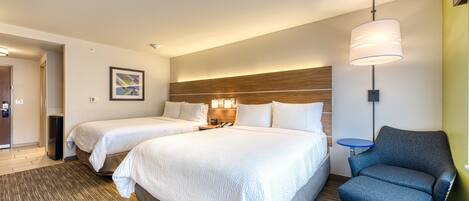 A hotel room with two beds, a desk, a chair, a lamp, and a framed picture on the wall.