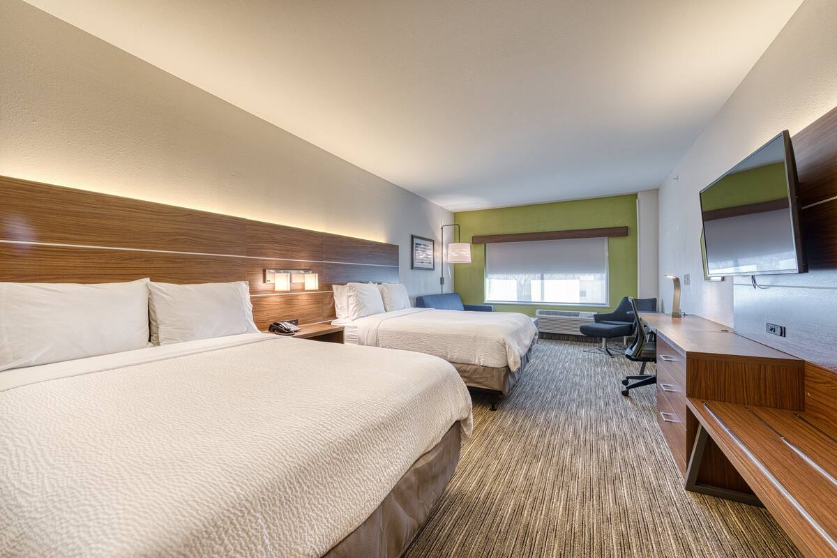 A hotel room with two beds, a desk, a chair, a flat-screen TV, and a window with a view.