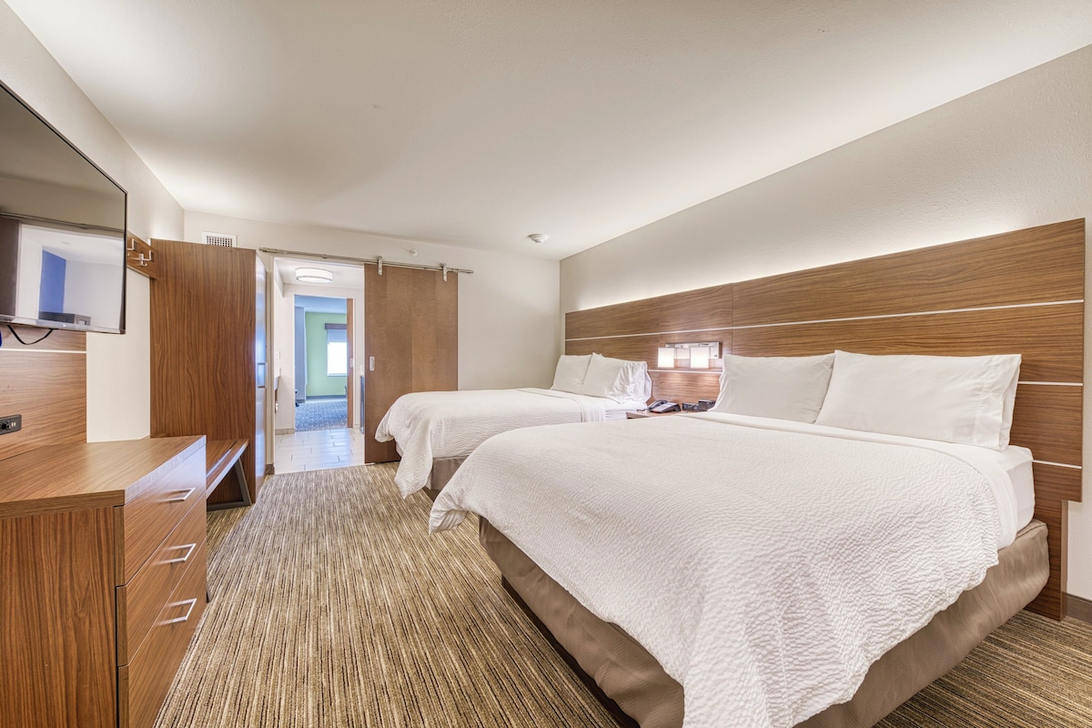 Habitación de hotel con dos camas, un aparador de madera, un televisor de pantalla plana y un espejo grande.