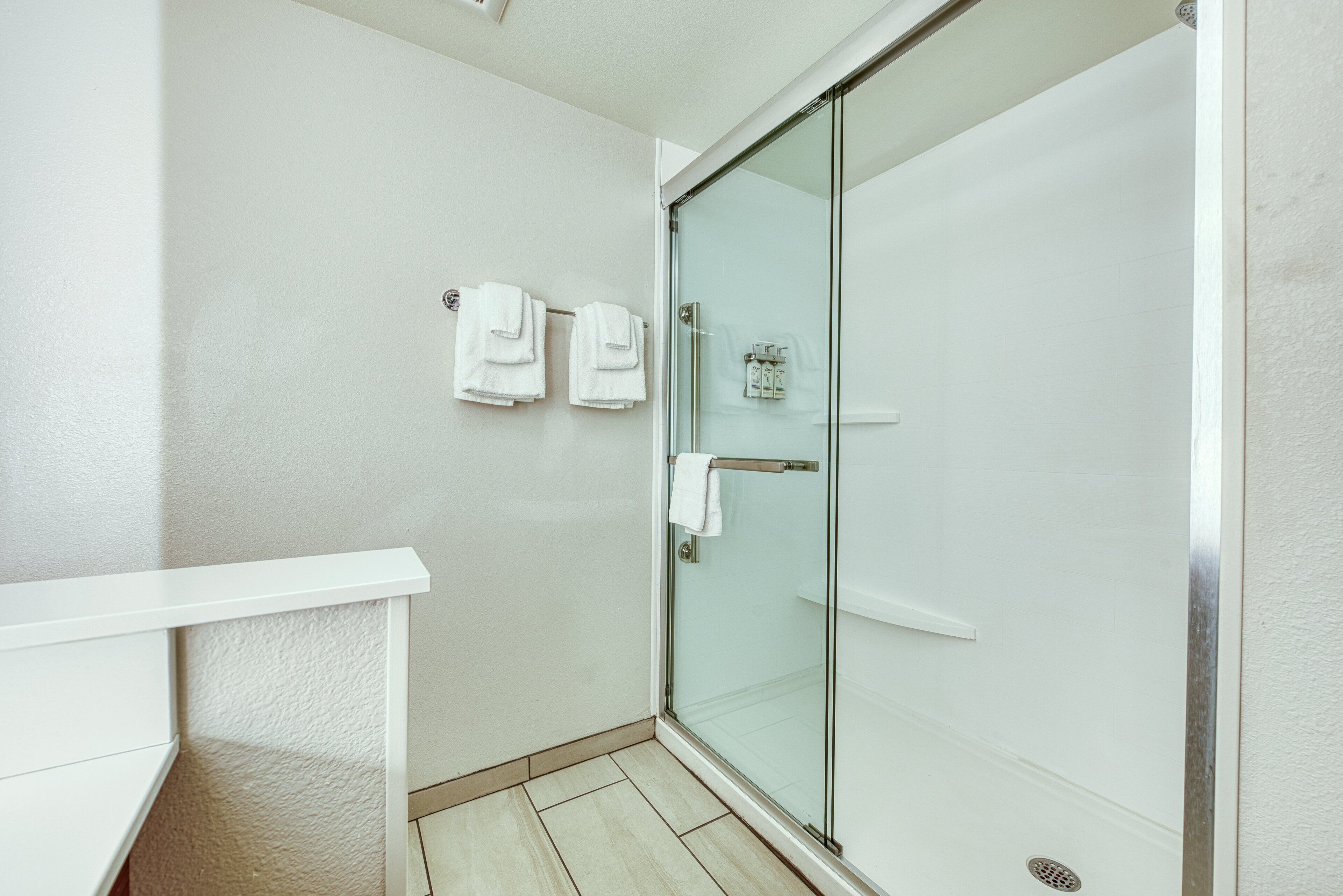 A modern bathroom with a glass shower enclosure, a white bathtub, and a white towel rack with two towels.