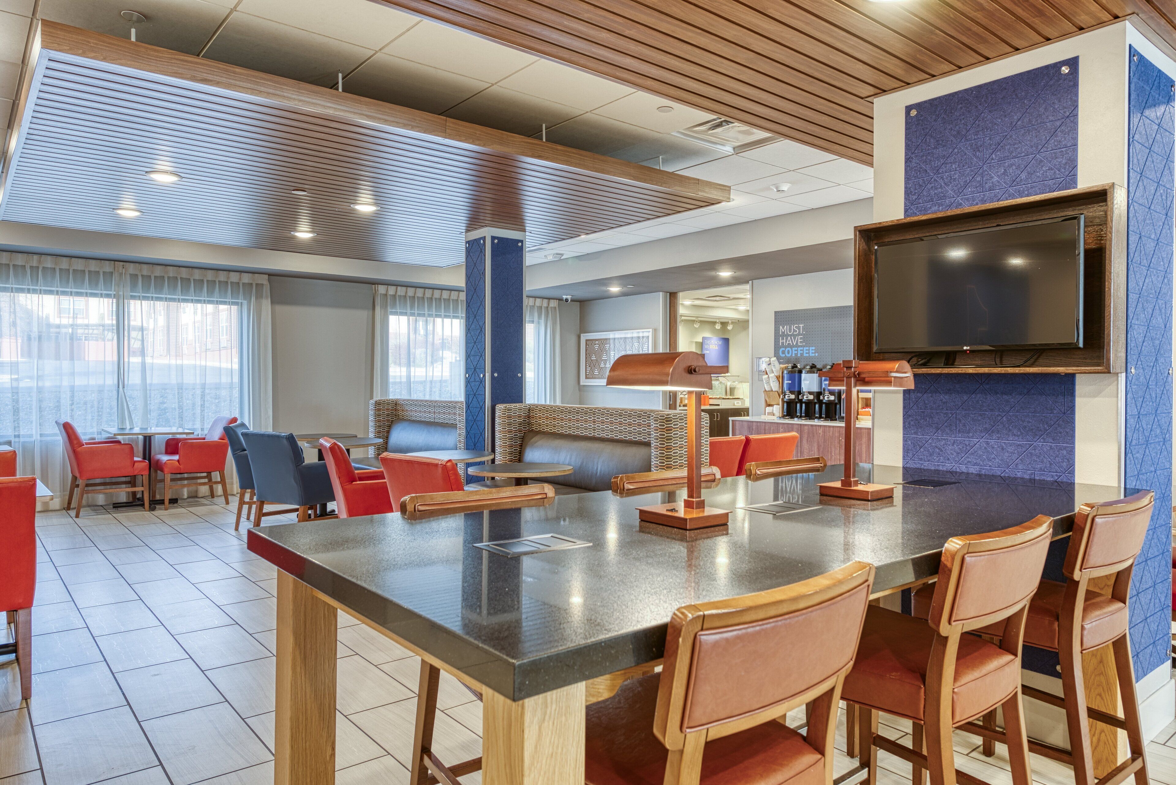 A modern hotel lobby with a large bar area, seating arrangements, and a television mounted on the wall.