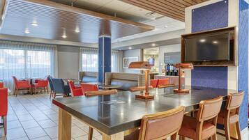 A modern hotel lobby with a large bar area, seating arrangements, and a television mounted on the wall.