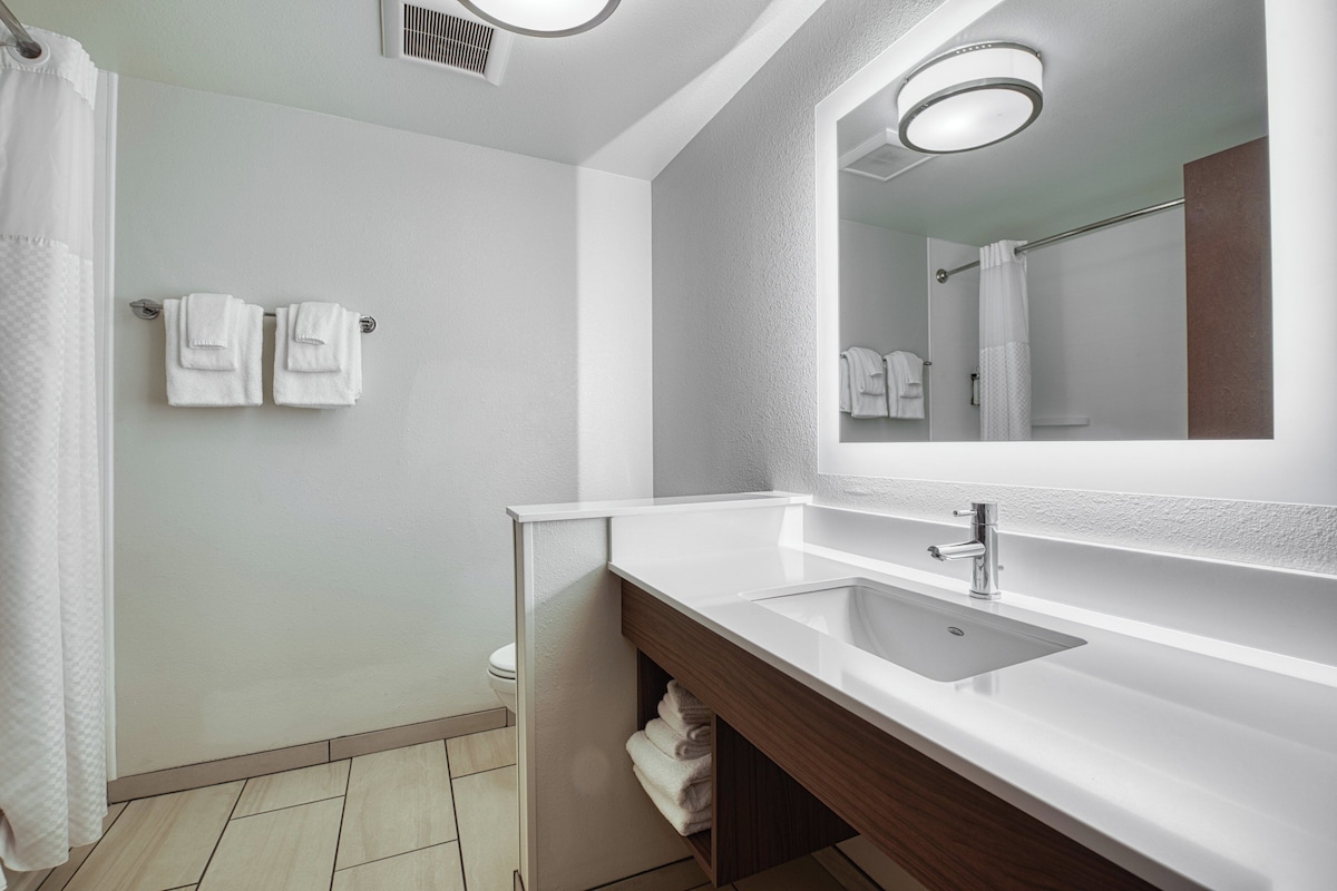 Un baño moderno con un lavabo blanco, un espejo y dos toallas colgadas en la pared.