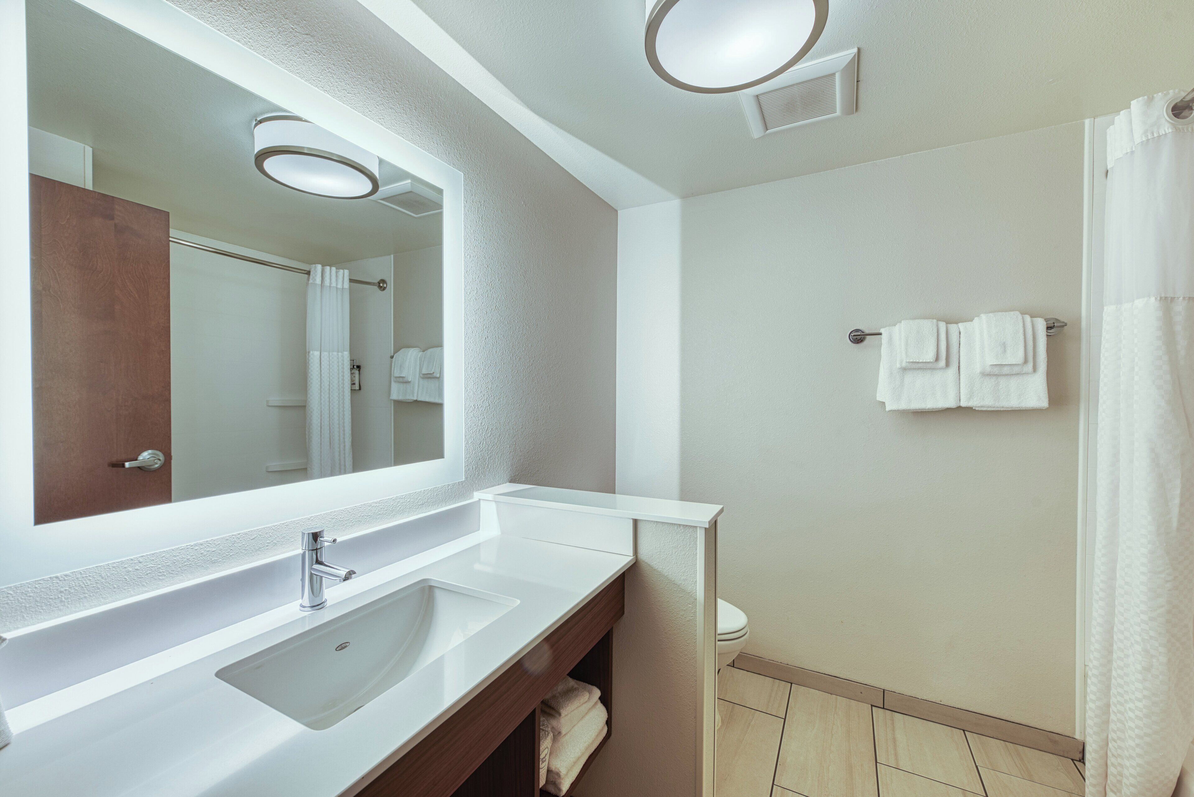 A bathroom with a large mirror, a sink, a toilet, and a shower area.