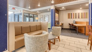 A modern lobby with a wooden ceiling, a seating area with a sofa and chairs, a reception desk, and a colorful wall art piece.