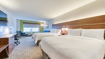 A hotel room with two beds, a desk, a chair, and a window with blinds.