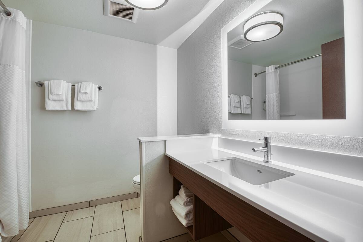 A modern bathroom with a white sink, a mirror, and two towels hanging on the wall.