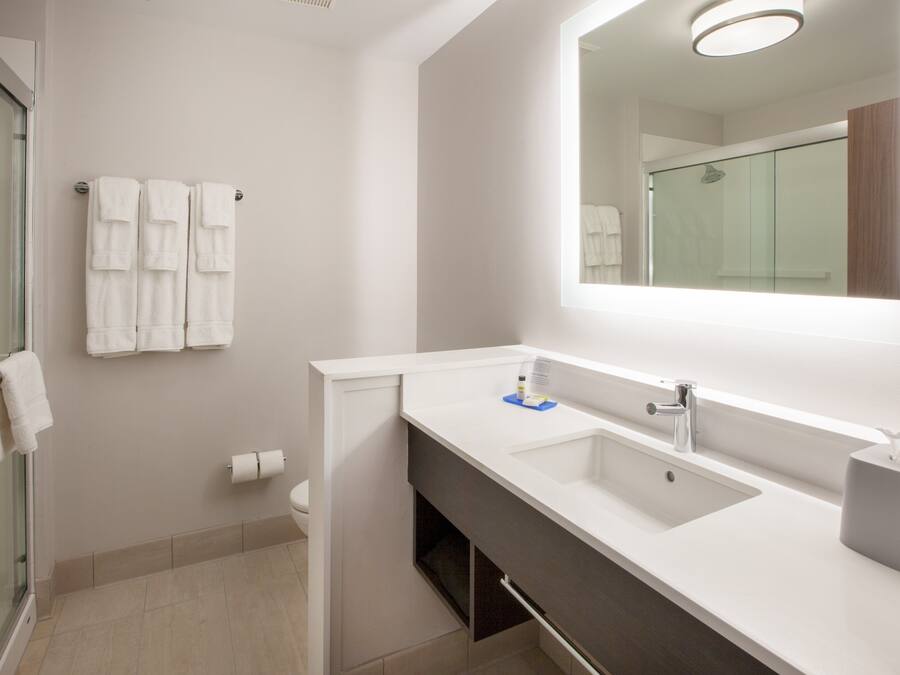 A modern bathroom with a glass shower enclosure, a white sink with a mirror above it, and two white towels hanging on a rack.