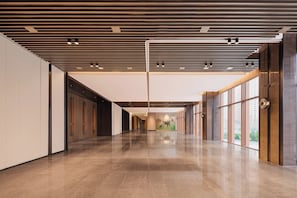 Um corredor amplo com piso lustroso, design moderno no teto e grandes janelas com vista.