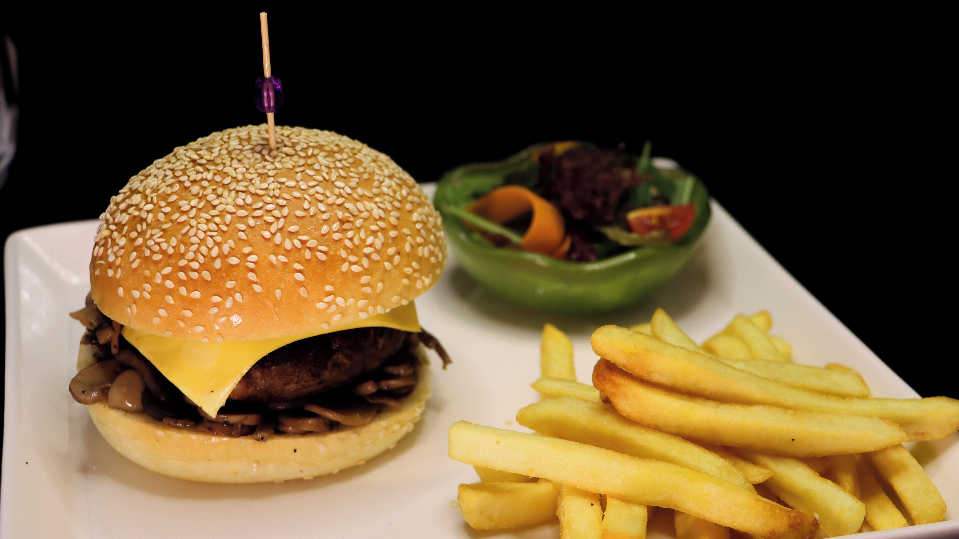 A hamburger with a sesame seed bun, a side of French fries, and a green bowl of salad.