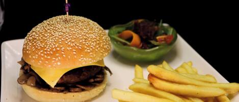 A hamburger with a sesame seed bun, a side of French fries, and a green bowl of salad.
