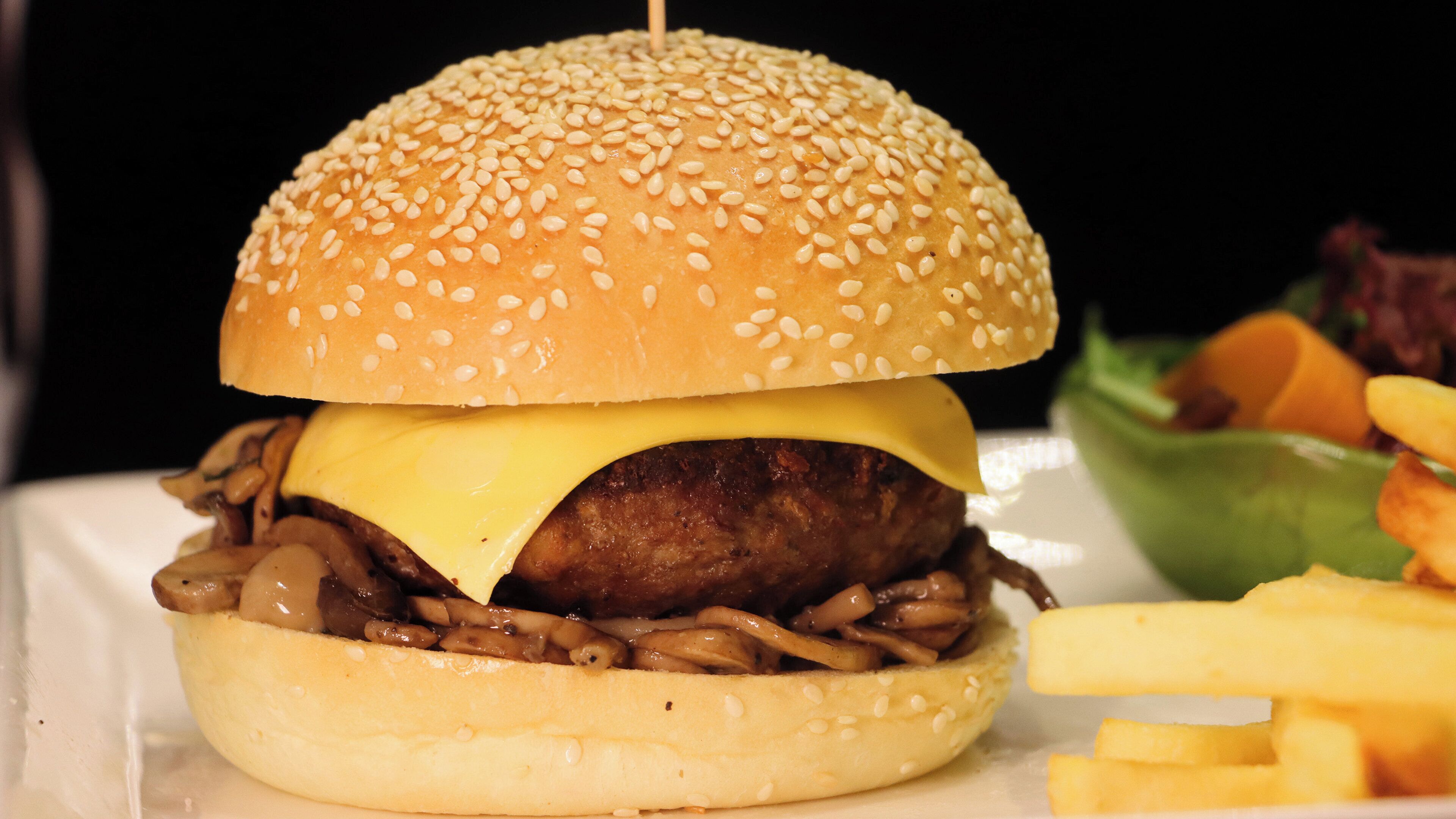 A hamburger with a sesame seed bun, cheese, and a beef patty, served with fries and a side salad.