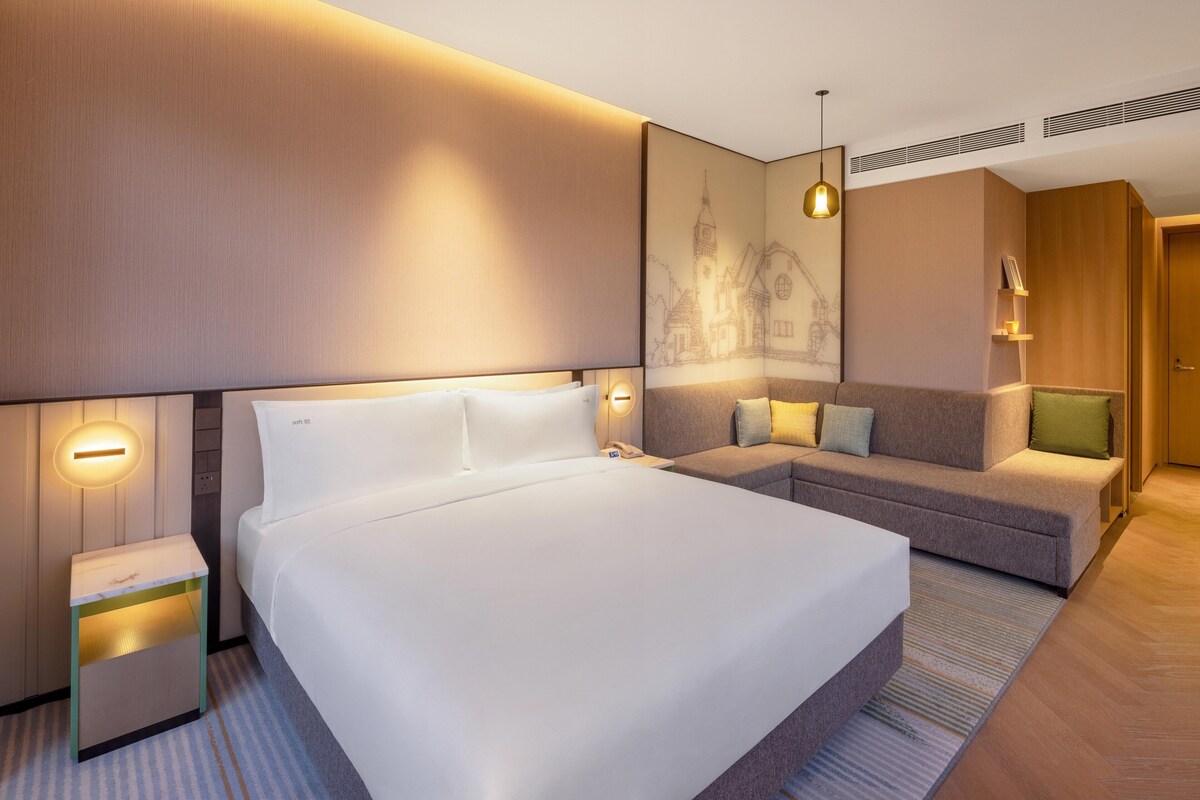 A modern hotel room with a large bed, a sofa, and a small table.