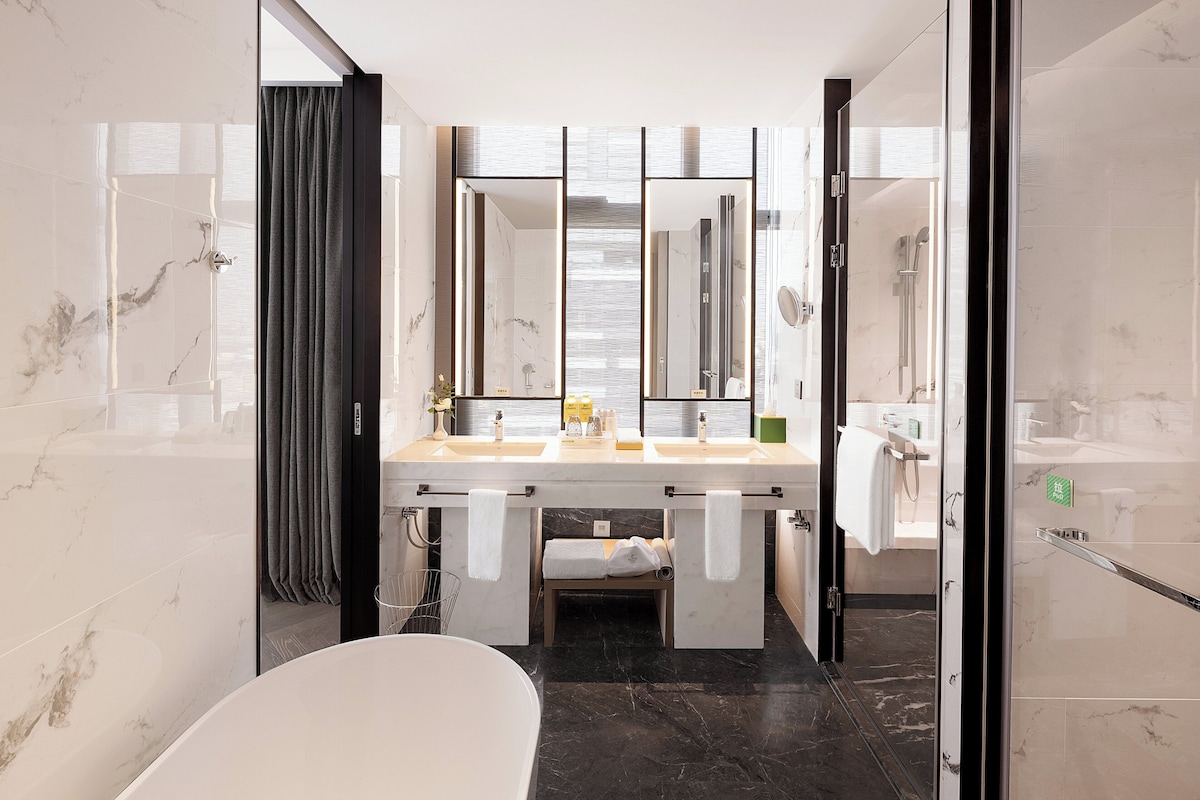 A modern bathroom with a large mirror, a bathtub, and a shower area.