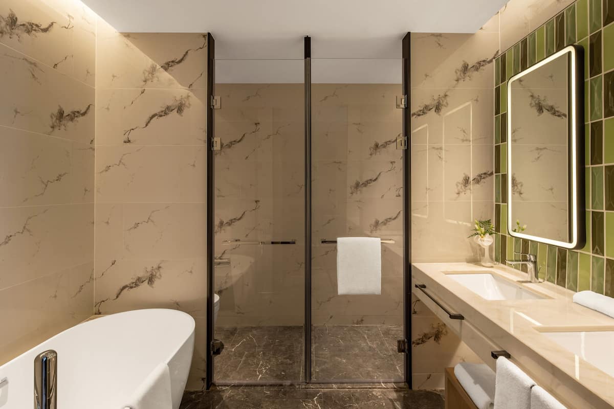A modern bathroom with a glass-enclosed shower, a white bathtub, and a vanity with a mirror.