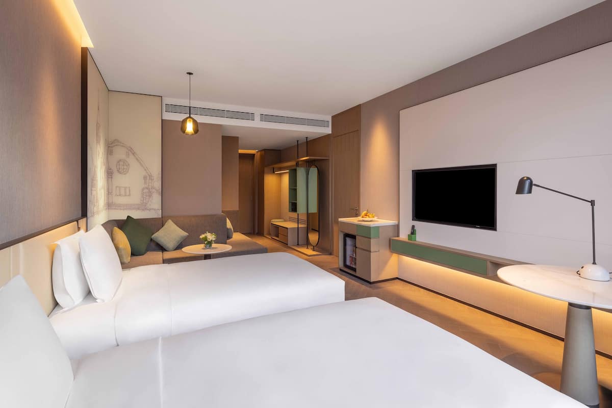 A modern hotel room with a large bed, a TV, a small table, and a bathroom with a mirror and sink.